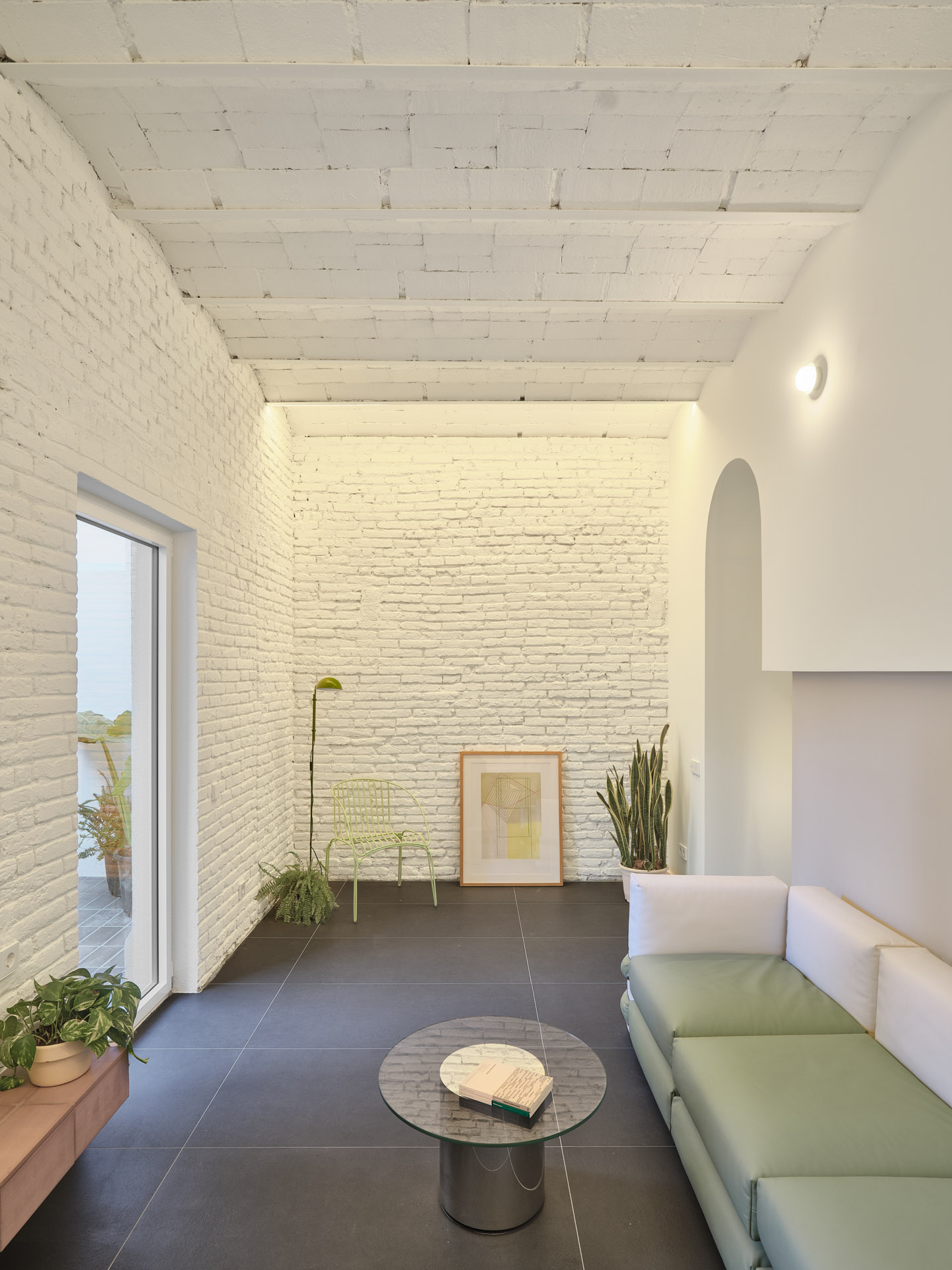 Living area in CRÜ’s “La Dolors” renovation, featuring whitewashed brick walls, an exposed ceramic ceiling, a Muller Van Severen modular sofa, and a glass coffee table facing the patio.
